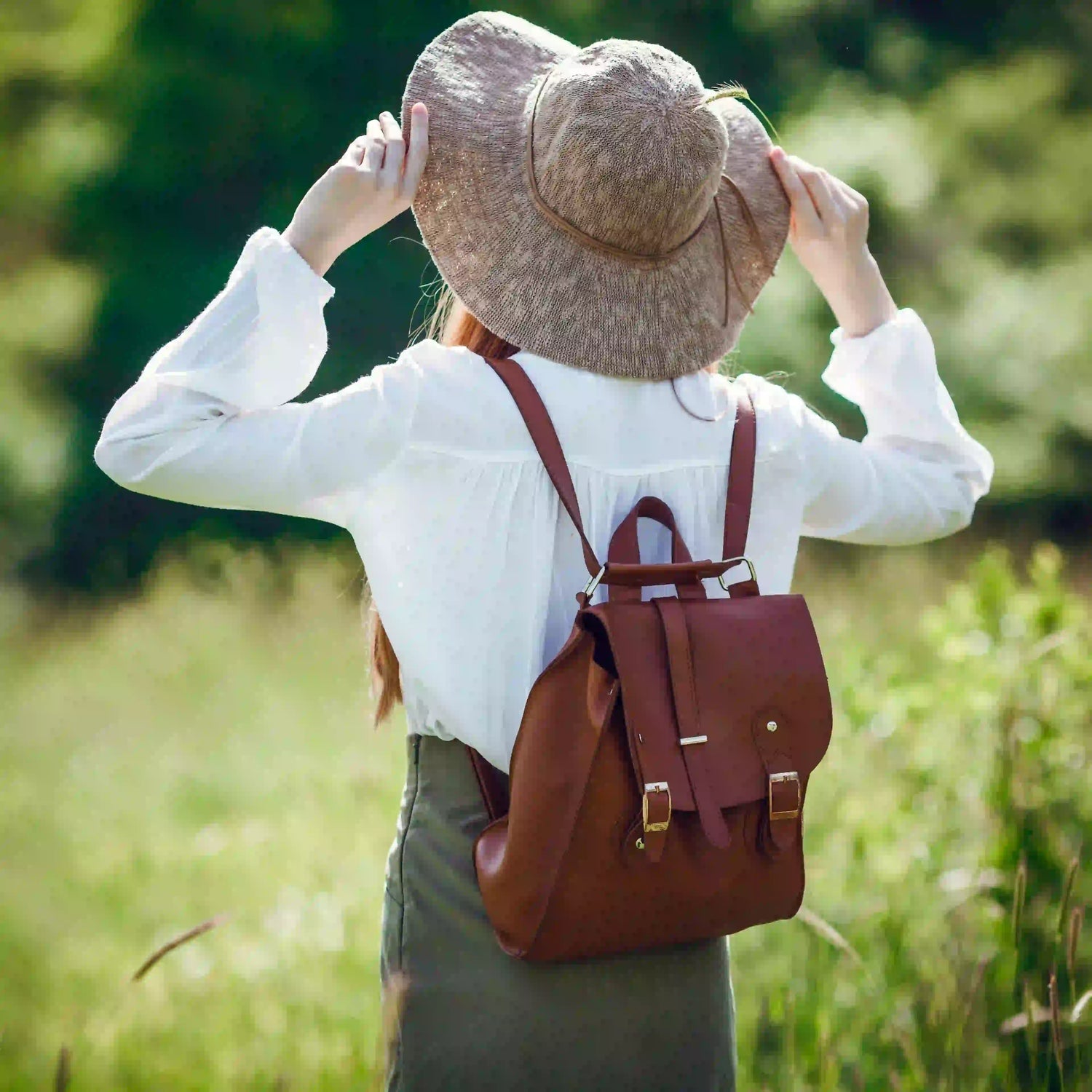 Kvinna med brun läderryggsäck och solhatt i naturen – elegant och praktisk ryggsäck för dam